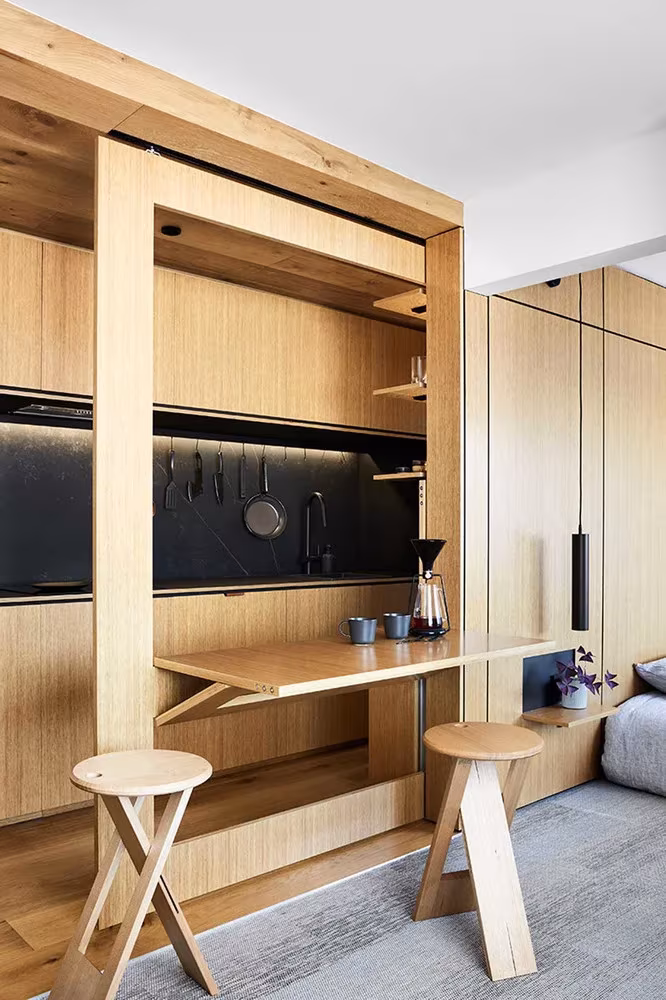 Mesa plegable y taburetes de madera desplegados ante la cocina del apartamento de Jack Chen