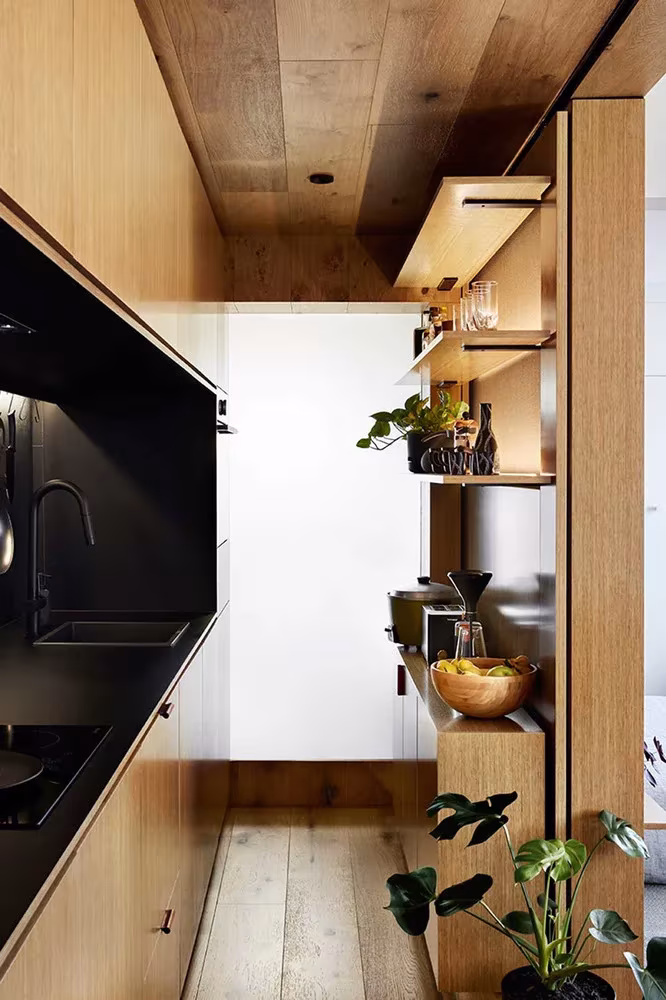 Estantes de roble y cocina negra junto al paso a la zona de descanso en el apartamento de Jack Chen