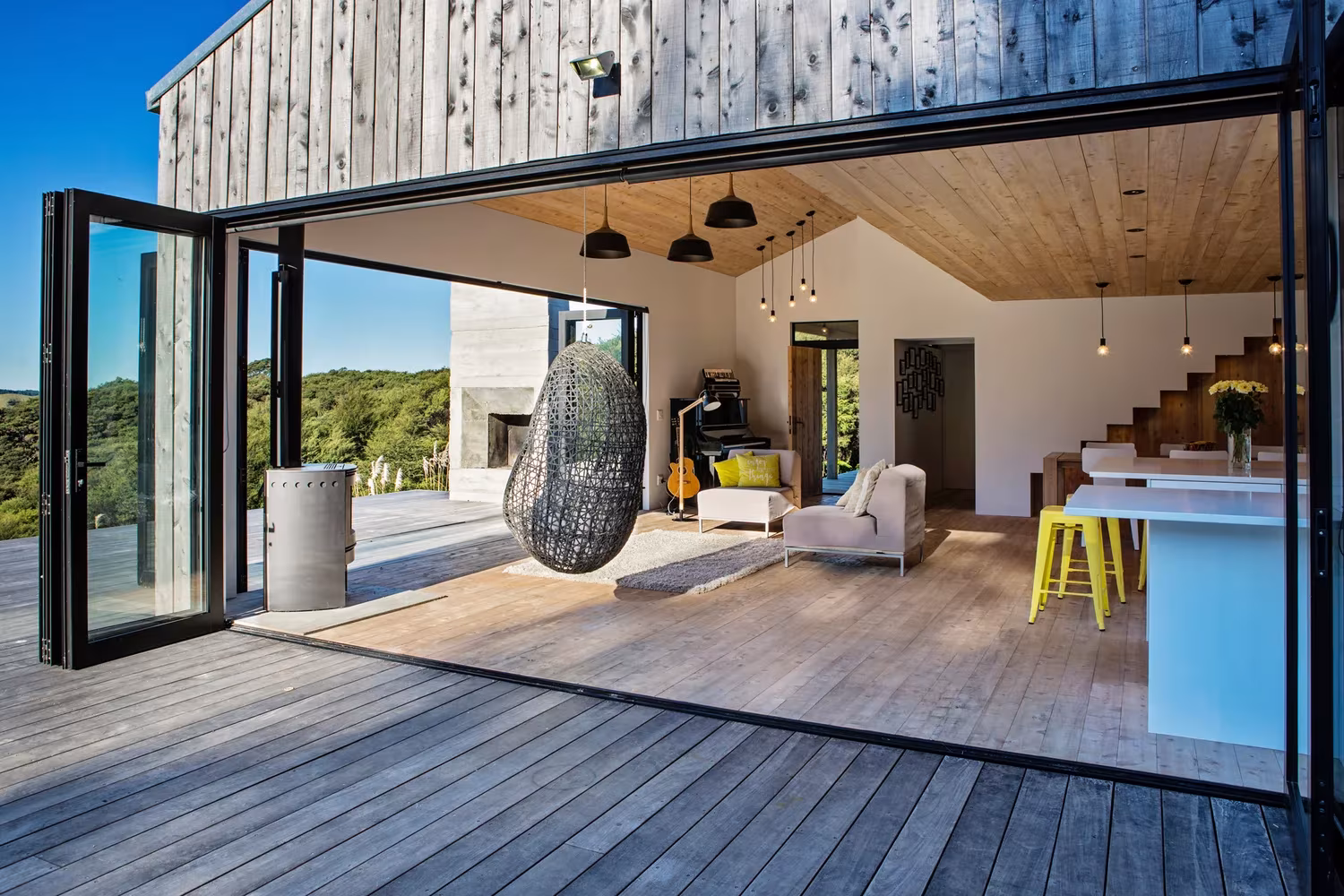 Salón de la Back Country House con puertas plegables abiertas a la terraza de madera y el sillón colgante