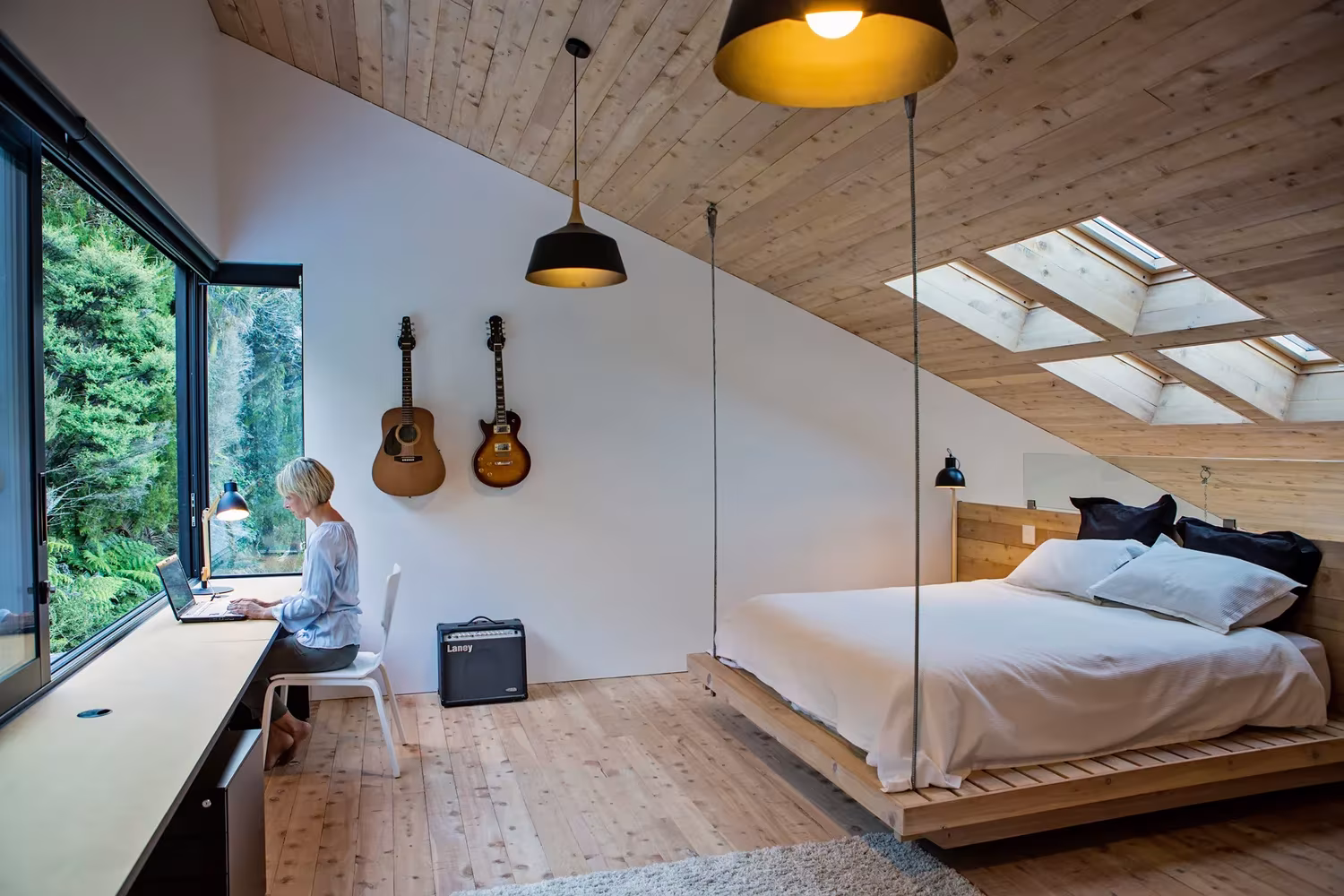 Dormitorio con cama suspendida, escritorio bajo la ventana y guitarras en la pared de la Back Country House