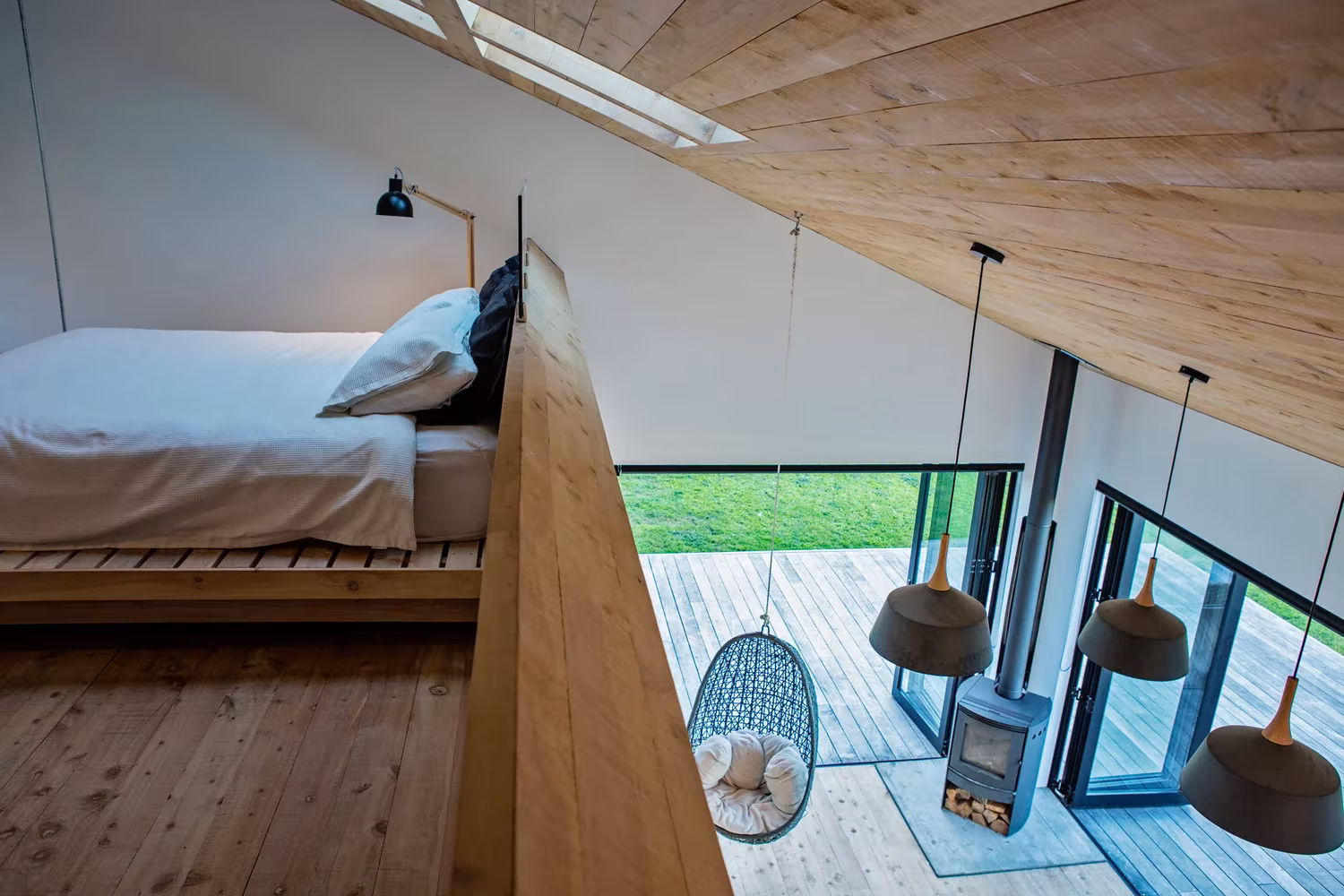 Dormitorio en altillo de la Back Country House con cubierta de madera y estufa negra junto a la terraza