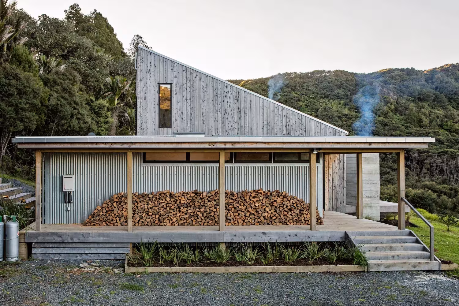Porche cubierto con leña apilada y fachada de madera inclinada de la Back Country House de LTD
