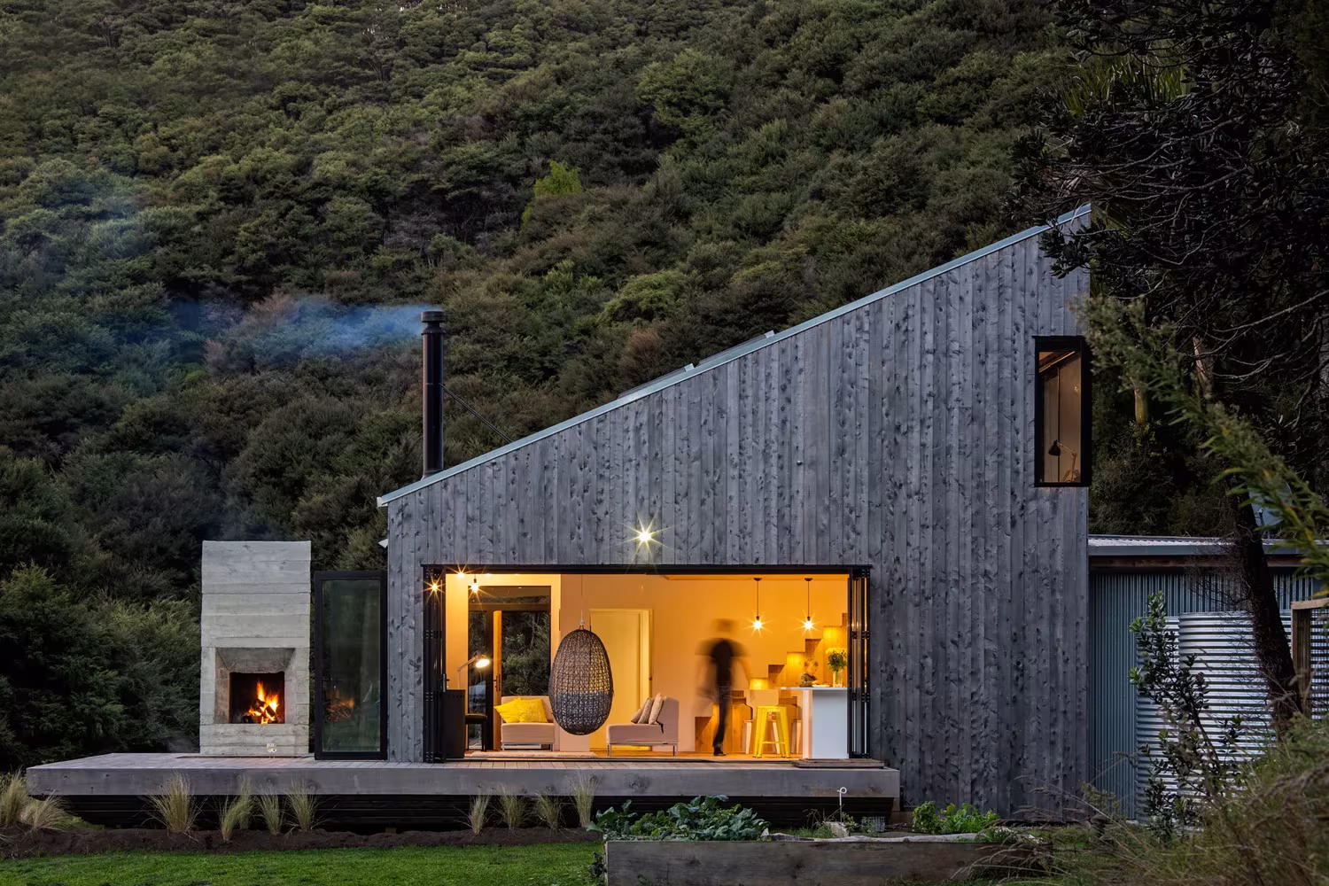 Back Country House de LTD Architectural Design Studio al anochecer, con chimenea exenta, junto a Puhoi