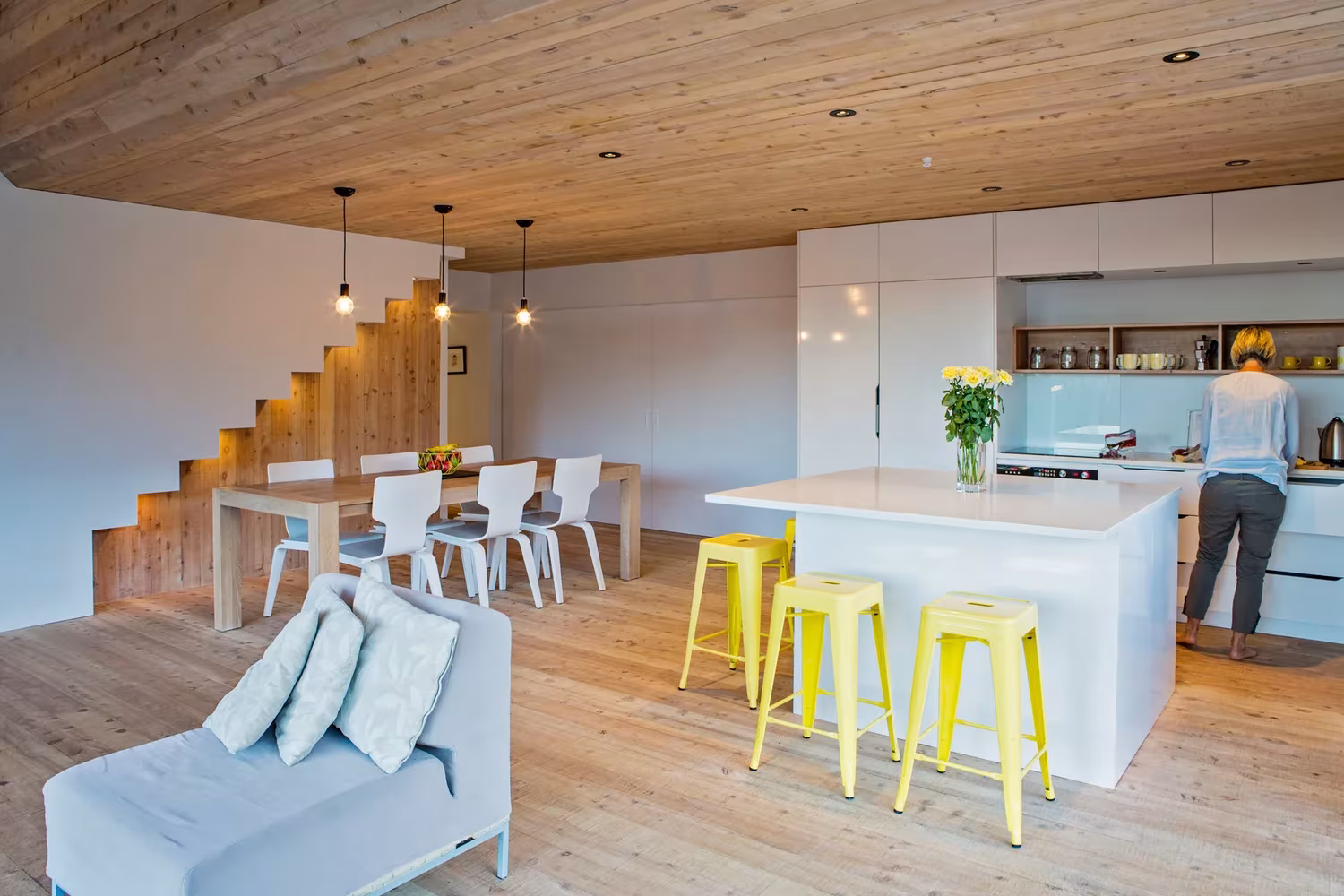 Cocina con isla blanca, taburetes amarillos y comedor bajo el techo de madera de la Back Country House
