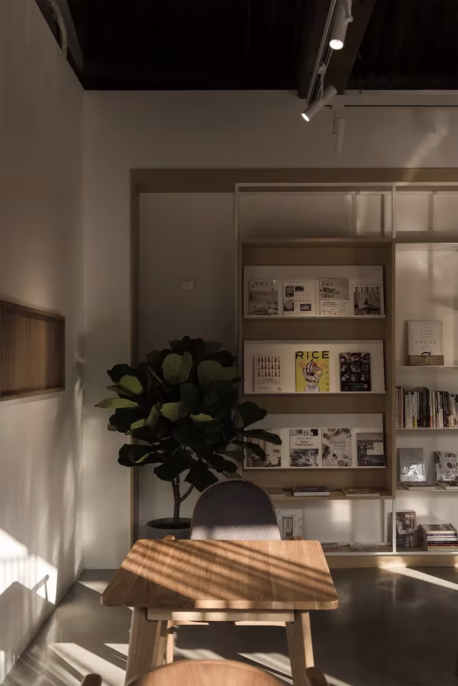 Estantería con libros de diseño, ficus y mesa de madera en la sala de Spring Whispers, en Pekín