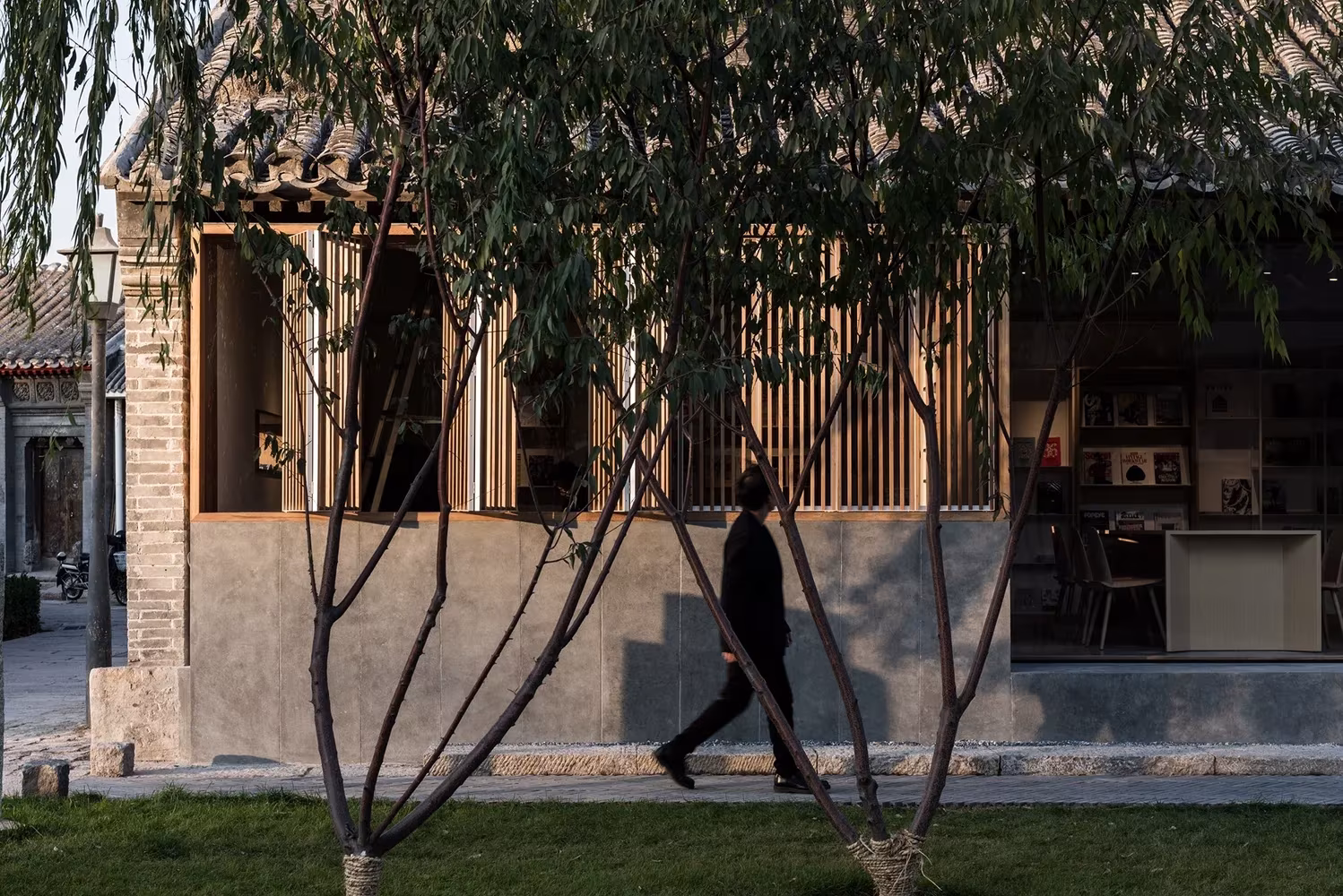 Fachada de madera y celosía del club Spring Whispers vista entre los árboles del patio, en un hutong de Pekín