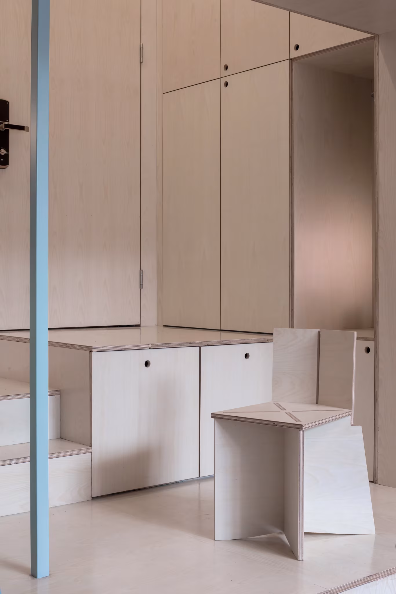 Vestíbulo de Atelier tao+c con armarios de madera clara, escalones de almacenaje y un taburete