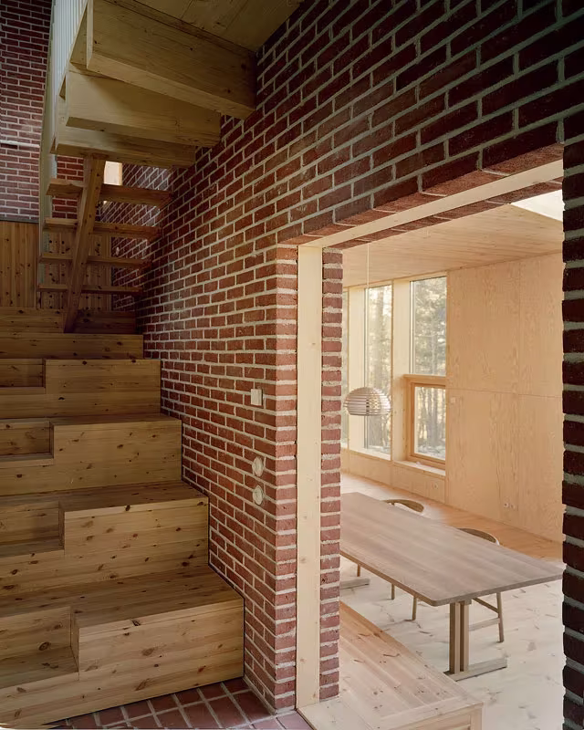 Escalera de madera junto al muro de ladrillo rojo y paso a la sala en la Villa Idun-Lee, Nacka