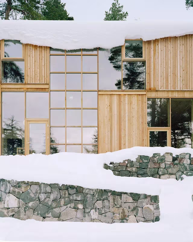 Fachada acristalada en cuadrícula de la Villa Idun-Lee con nieve y un muro de piedra en primer término