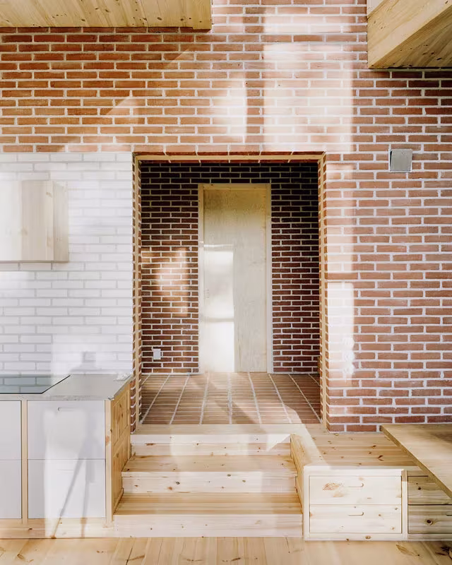 Estancia con muro de ladrillo rojo y blanco, hueco con peldaños y cocina de madera en la Villa Idun-Lee