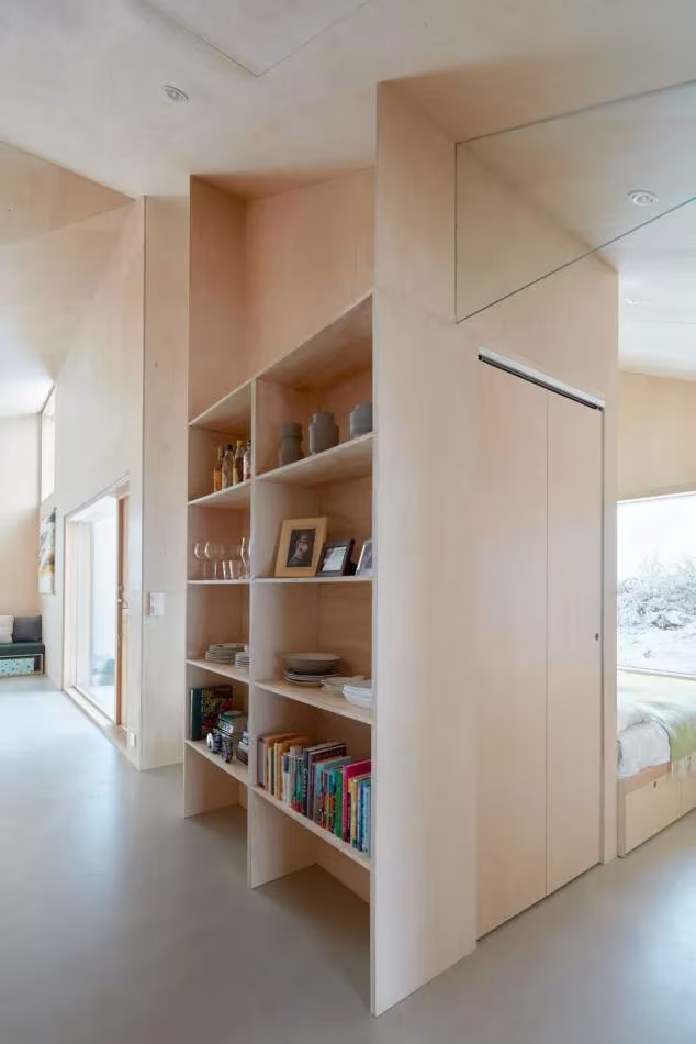 Mueble-librería de madera clara que separa la sala de los dormitorios en la Mylla Hytte de Mork Ulnes