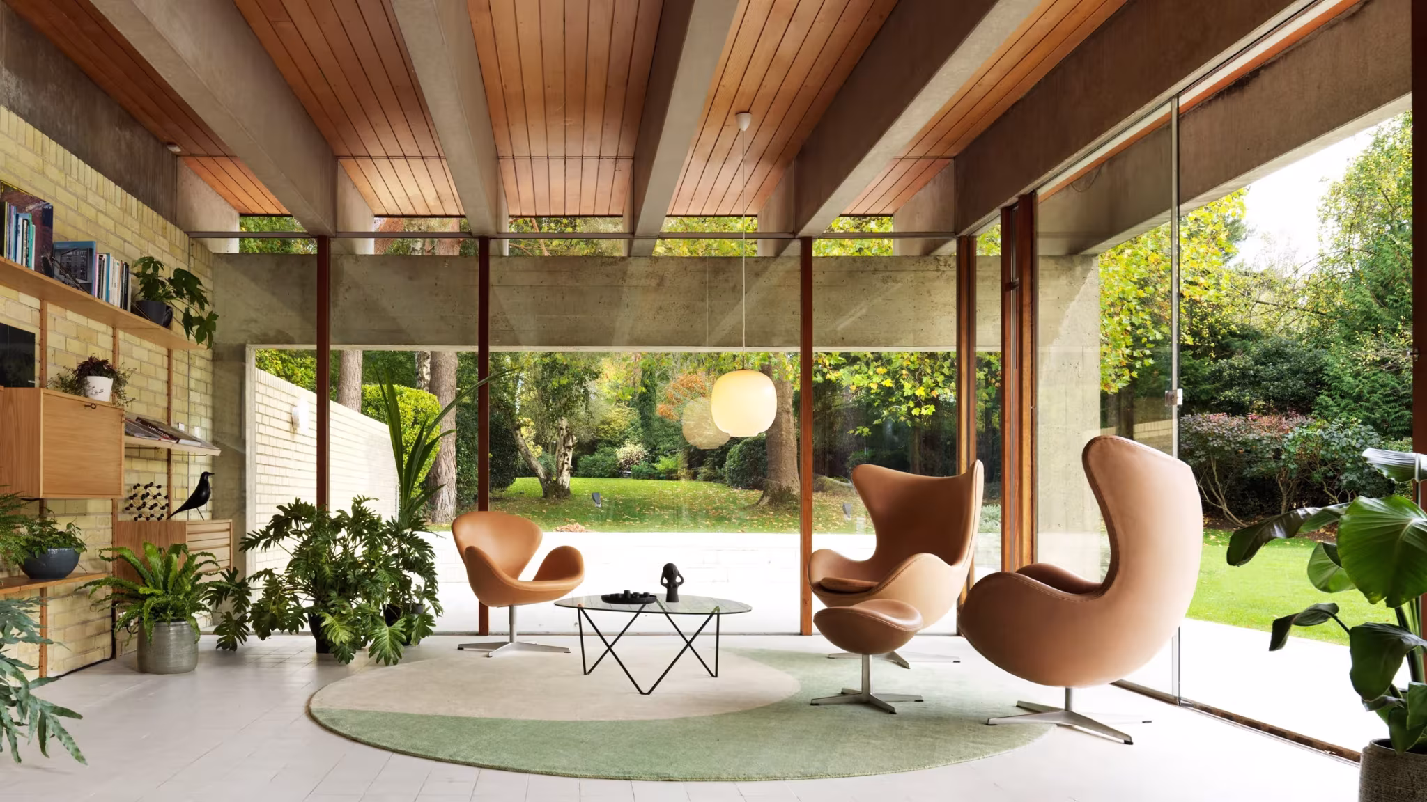 Sala de estar de la Ahm House, con techo de vigas de madera, sillones Egg y vidrio hacia el jardín