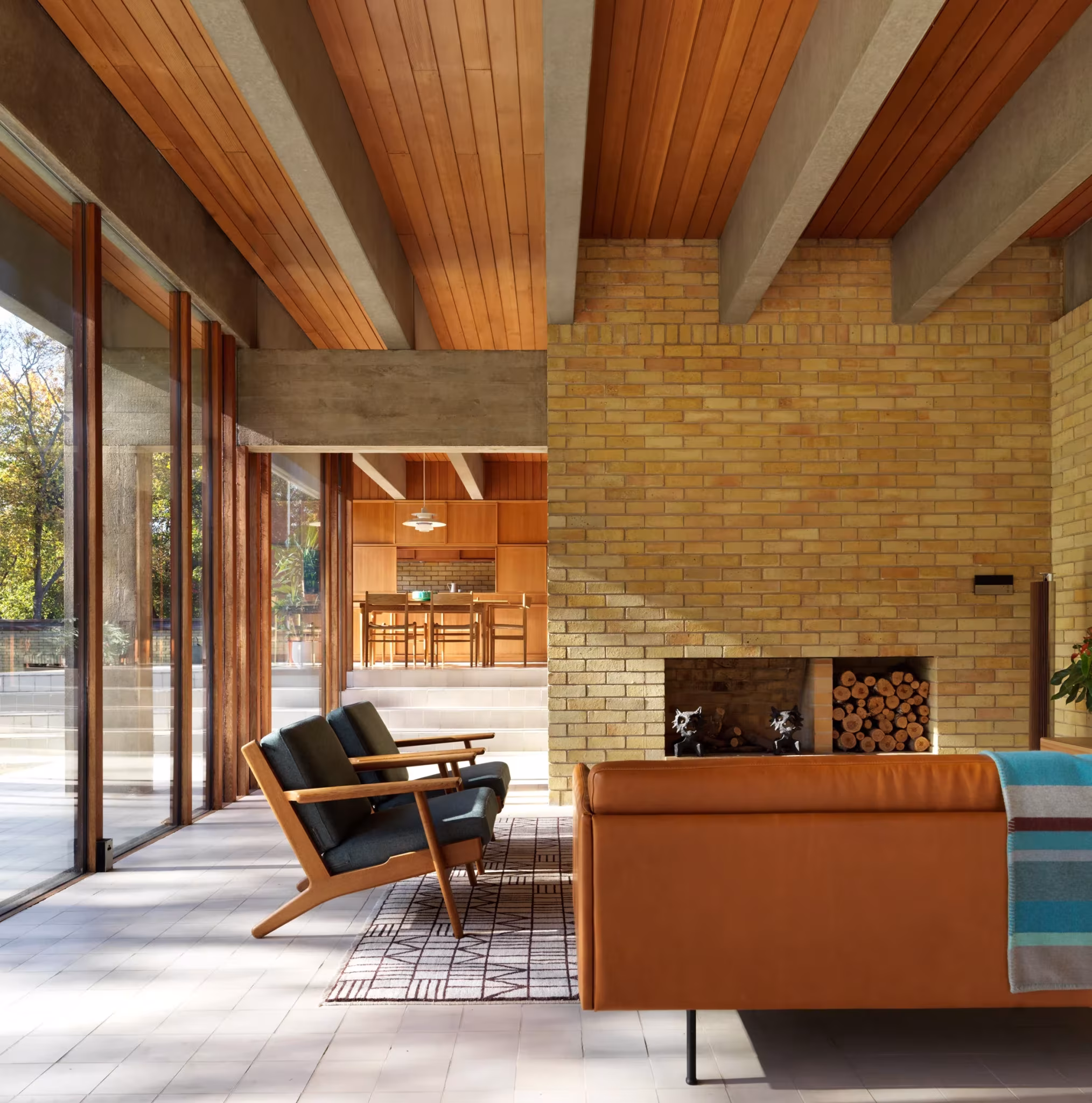 Salón de la Ahm House con chimenea de ladrillo, techo de madera y sillones junto a la cristalera, de Jørn Utzon