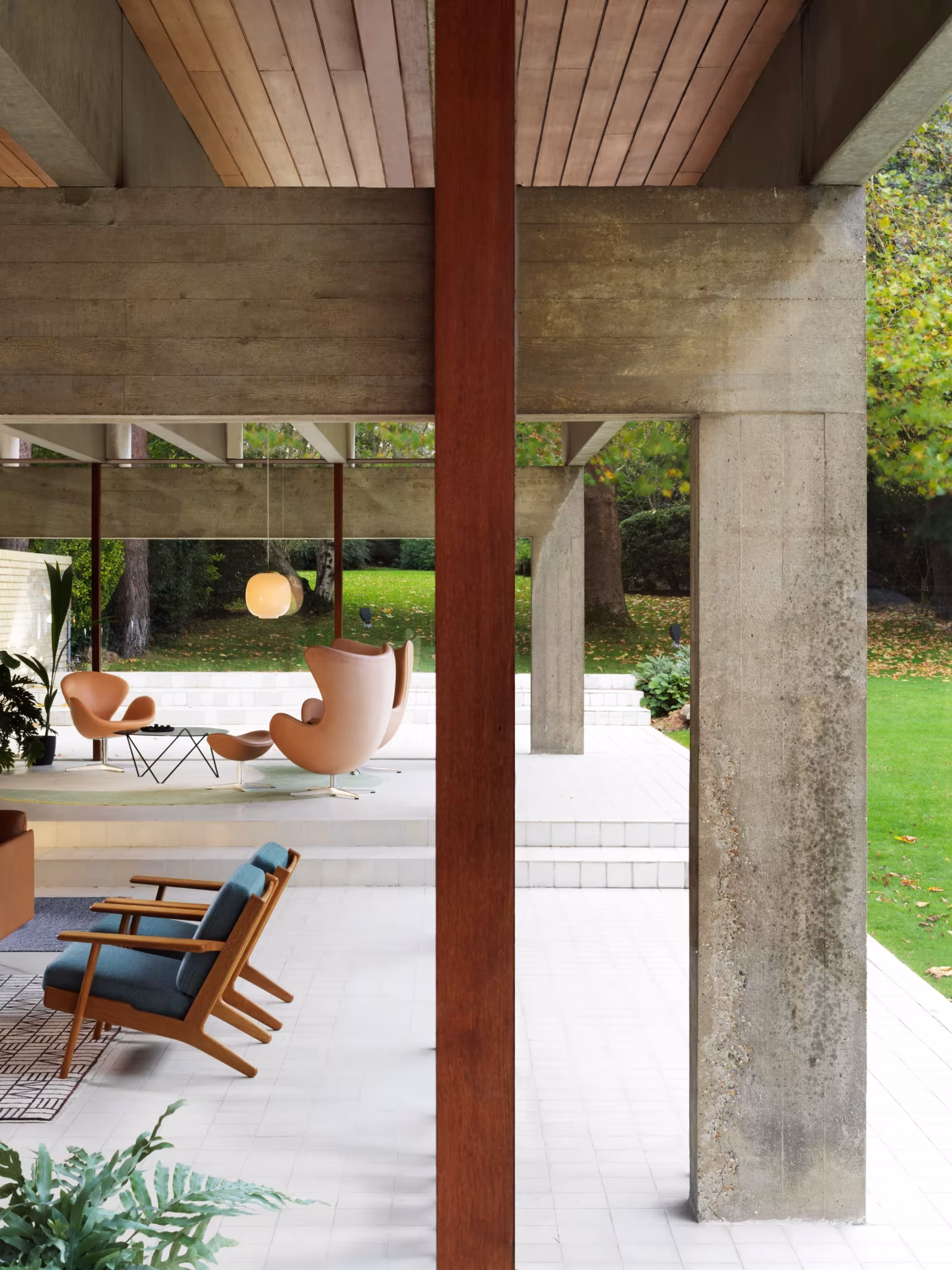 Pilar de acero corten entre pórticos de hormigón y sillones frente al jardín en la Ahm House renovada por Coppin Dockray
