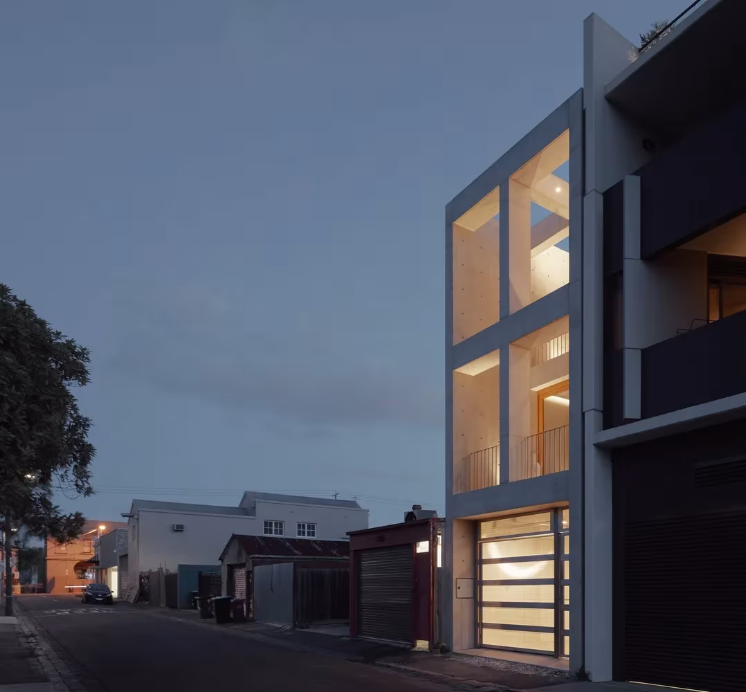 Skinny House de Oliver du Puy Architects al anochecer, con la fachada acristalada iluminada sobre el callejón, Melbourne