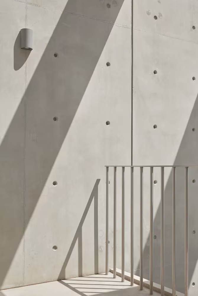 Muro de hormigón visto con sombras diagonales y barandilla metálica en la terraza de la Skinny House de Oliver du Puy