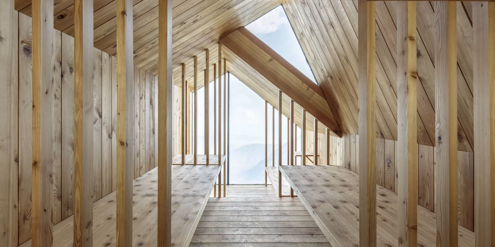 Interior de madera de alerce del refugio Skuta, con bancos corridos y gran ventana inclinada abierta a la montaña