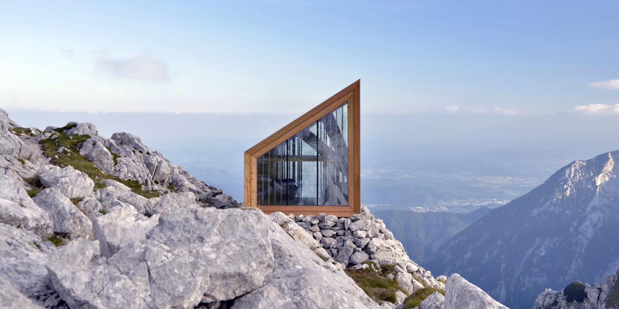 Ventana inclinada con marco de madera del refugio Skuta, asomada sobre la roca y el paisaje alpino de Eslovenia
