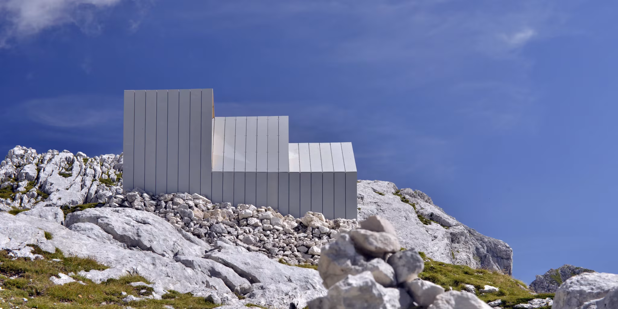 Fachada escalonada de paneles de fibra de vidrio del refugio Skuta de OFIS Arhitekti entre las rocas alpinas