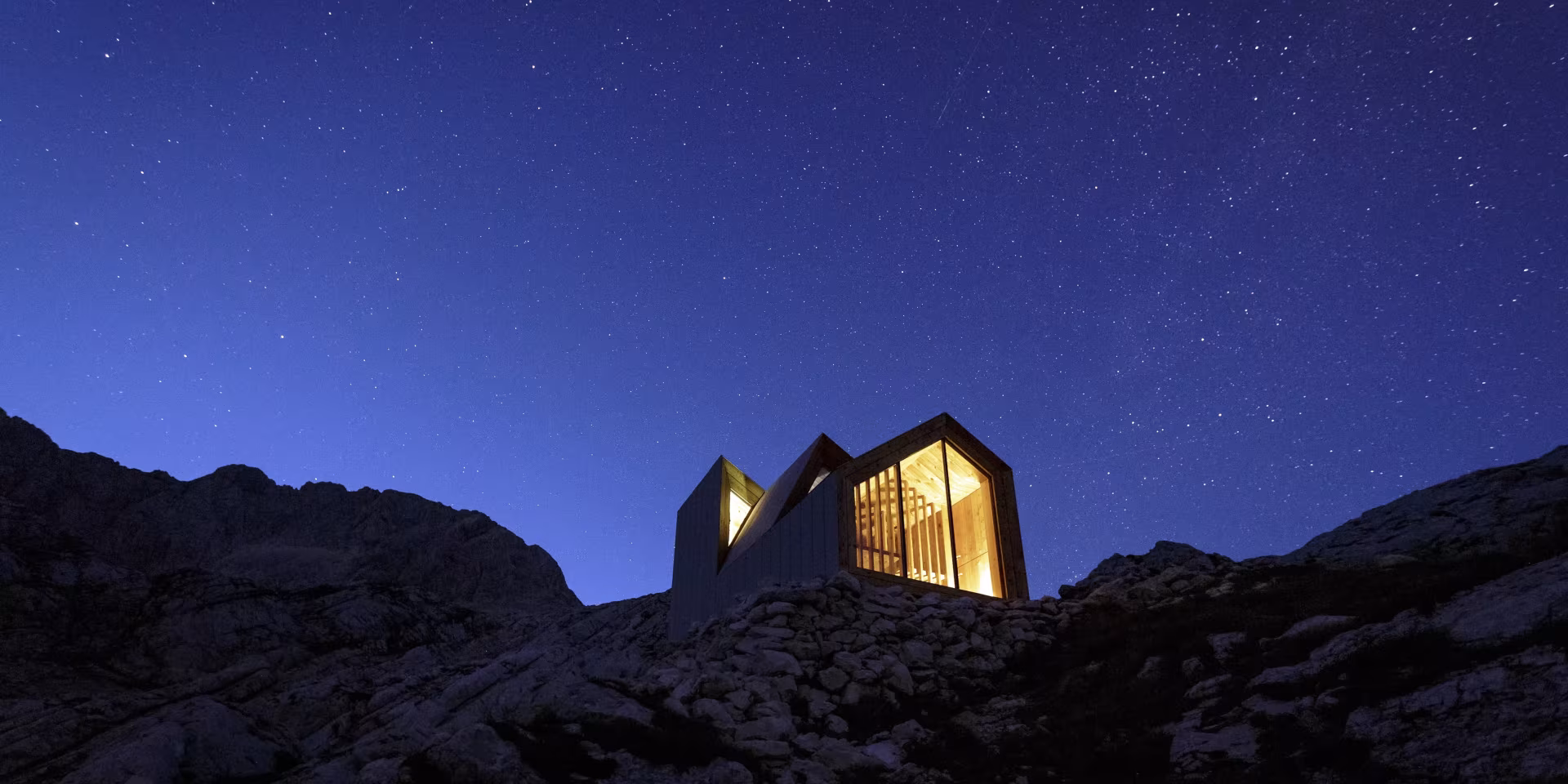 Refugio Skuta de OFIS Arhitekti con sus tres volúmenes iluminados bajo un cielo estrellado a 2.532 metros de altitud