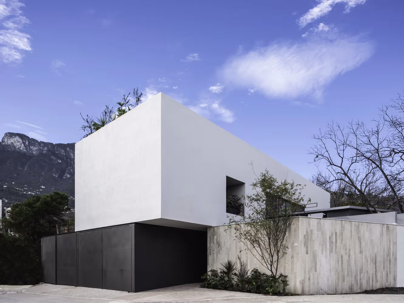 Volumen blanco en voladizo de Genius Loci sobre el basamento oscuro y el muro de piedra, con la sierra de Monterrey al fondo