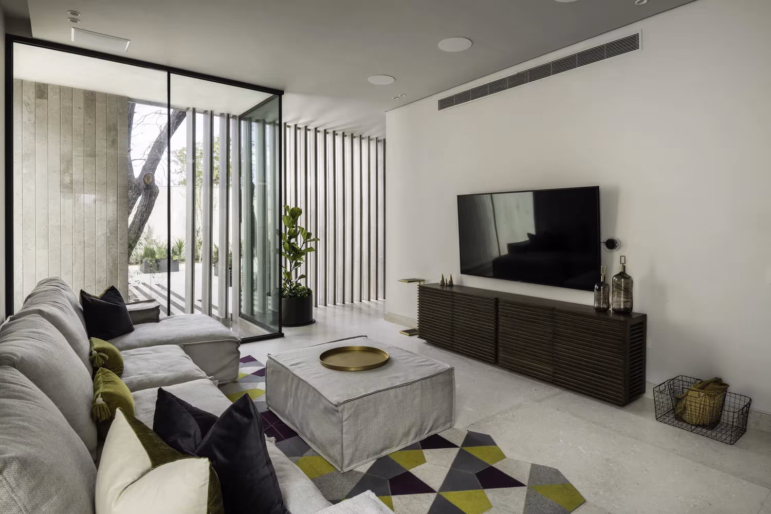 Sala de estar con sofás, celosía de lamas y cerramiento acristalado hacia el jardín en Genius Loci, Monterrey