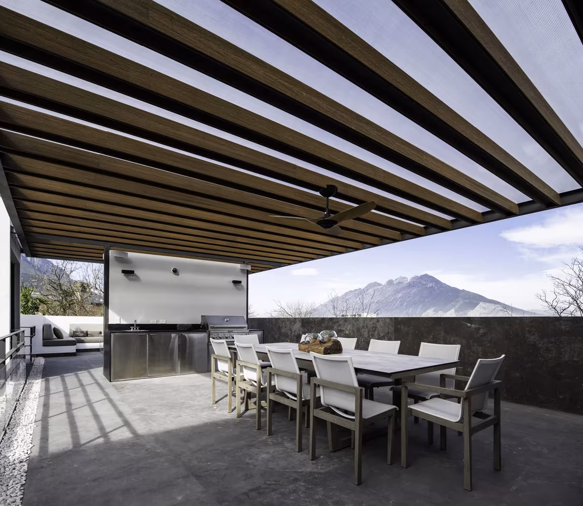 Terraza cubierta con pérgola de vigas de madera y comedor exterior frente a la montaña en Genius Loci, Monterrey