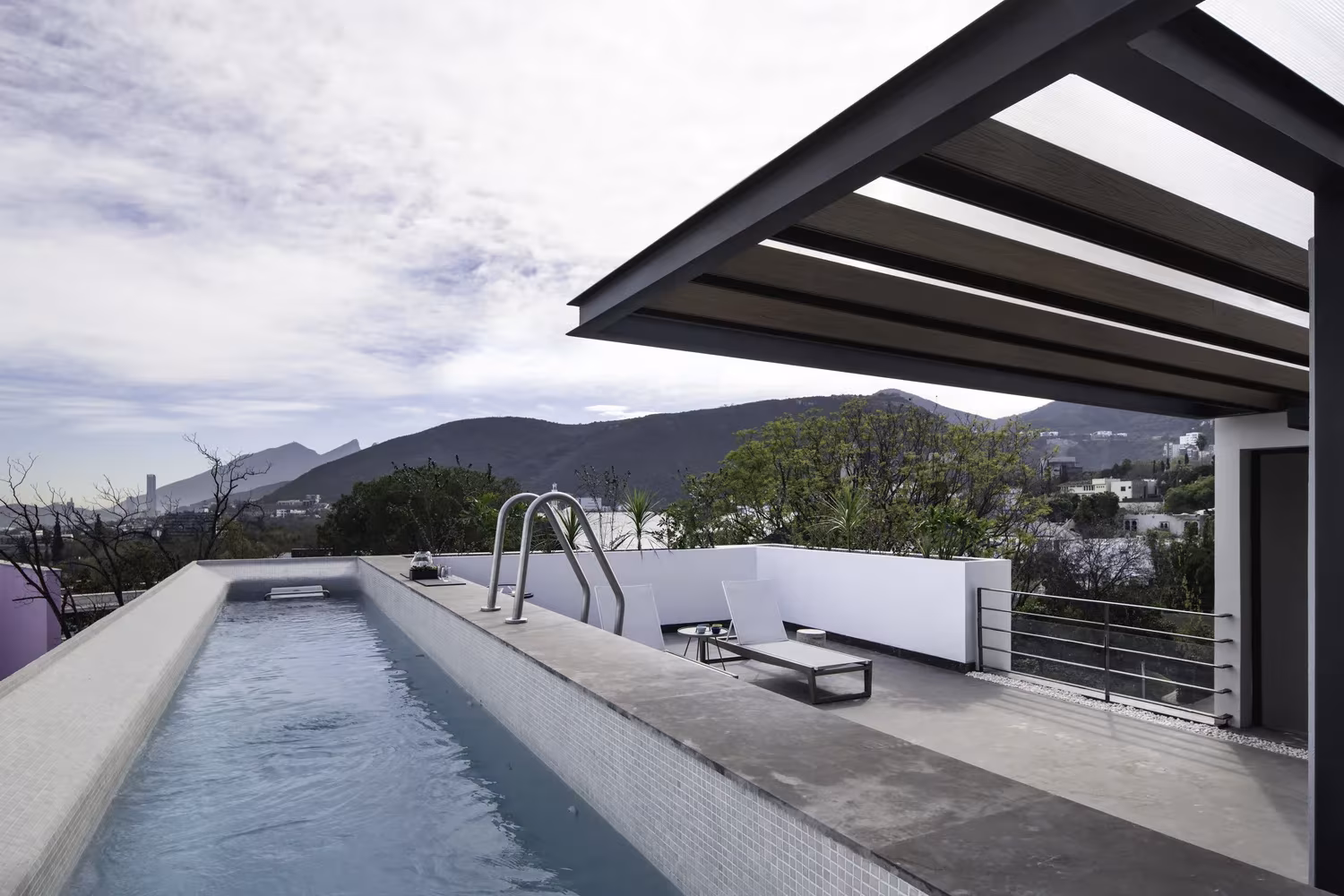 Piscina alargada de hormigón bajo una marquesina metálica con vistas a la sierra de Monterrey en Genius Loci