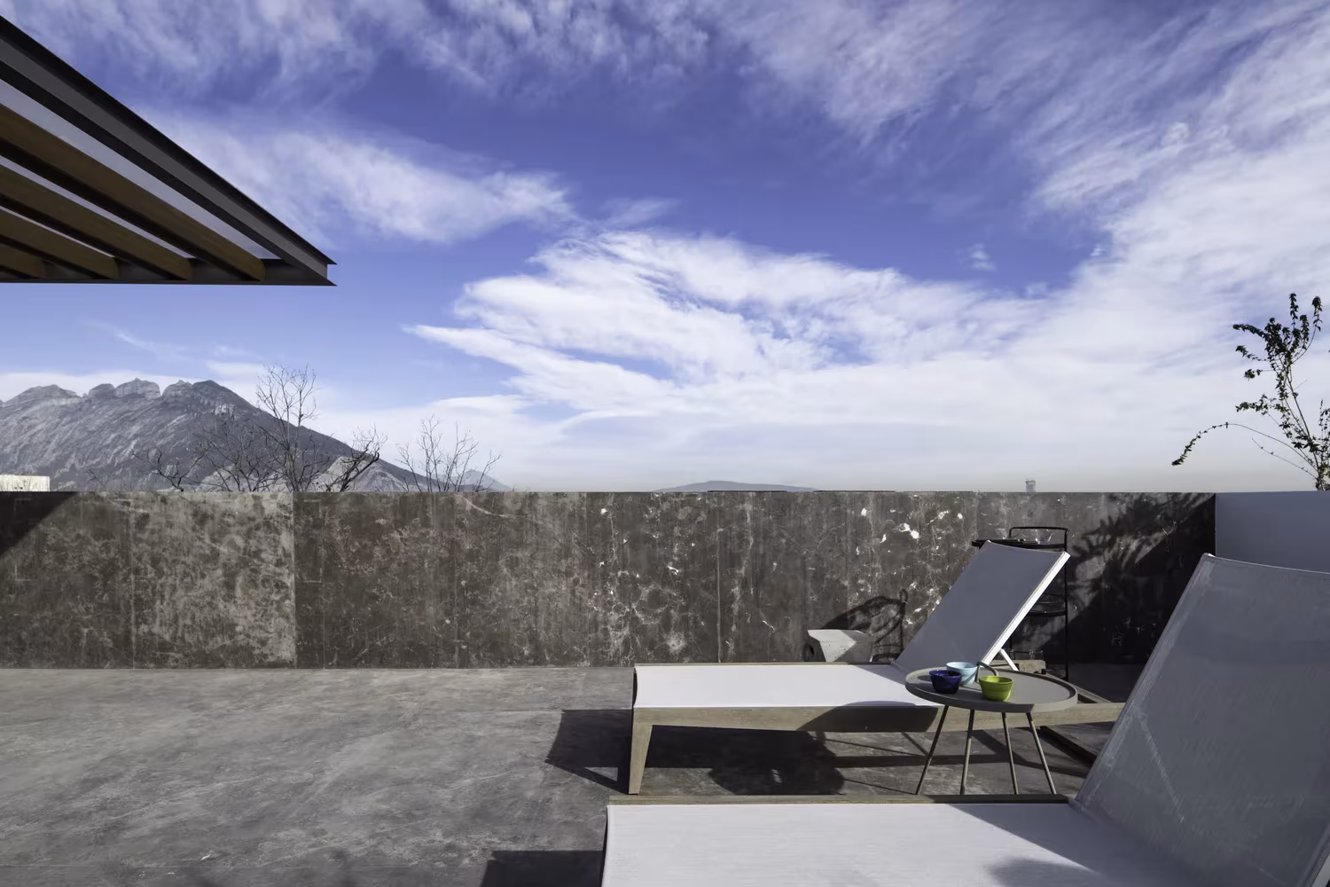 Azotea de Genius Loci con tumbonas sobre un pavimento de piedra y vistas a la sierra de Monterrey