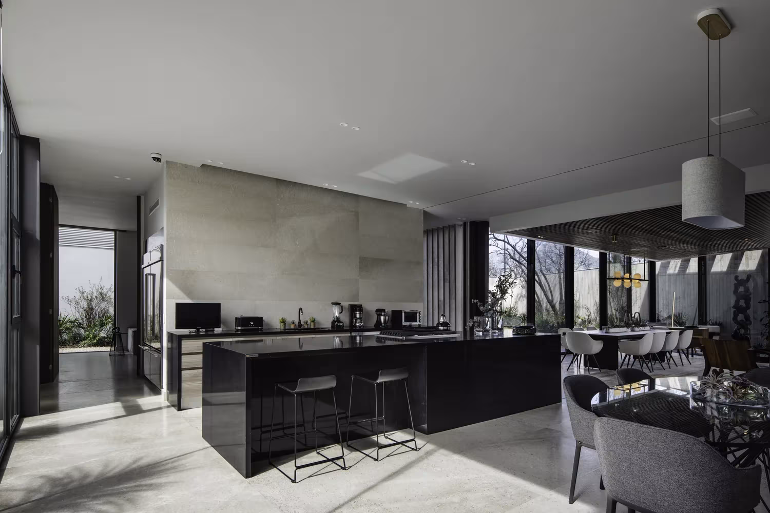 Cocina y comedor abiertos con isla negra y grandes ventanales hacia la montaña en Genius Loci de Tescala, Monterrey