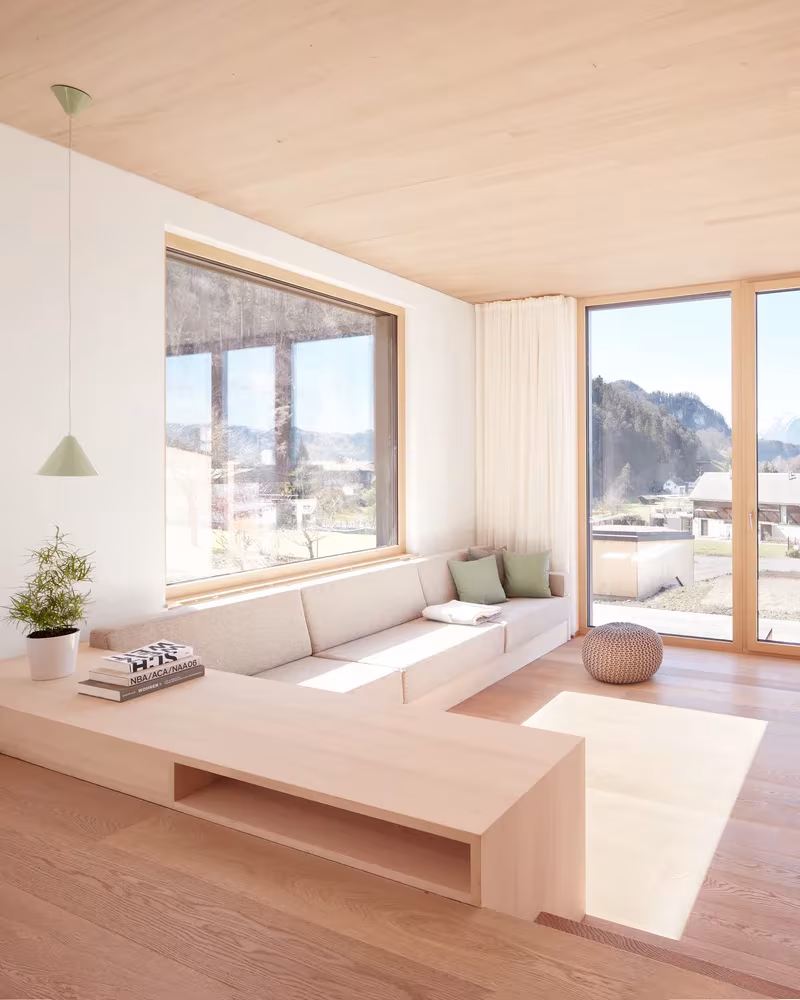 Rincón de estar con banco de madera y gran ventana abierta a las montañas en la casa de MWArchitekten, Vorarlberg