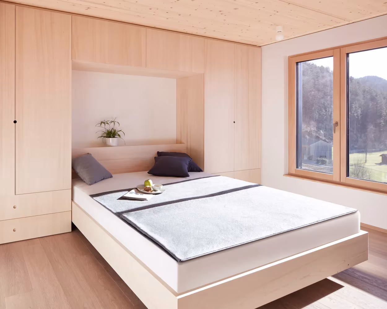 Dormitorio con cama sobre plataforma, armarios de madera empotrados y ventana al valle en la casa de Hohenems