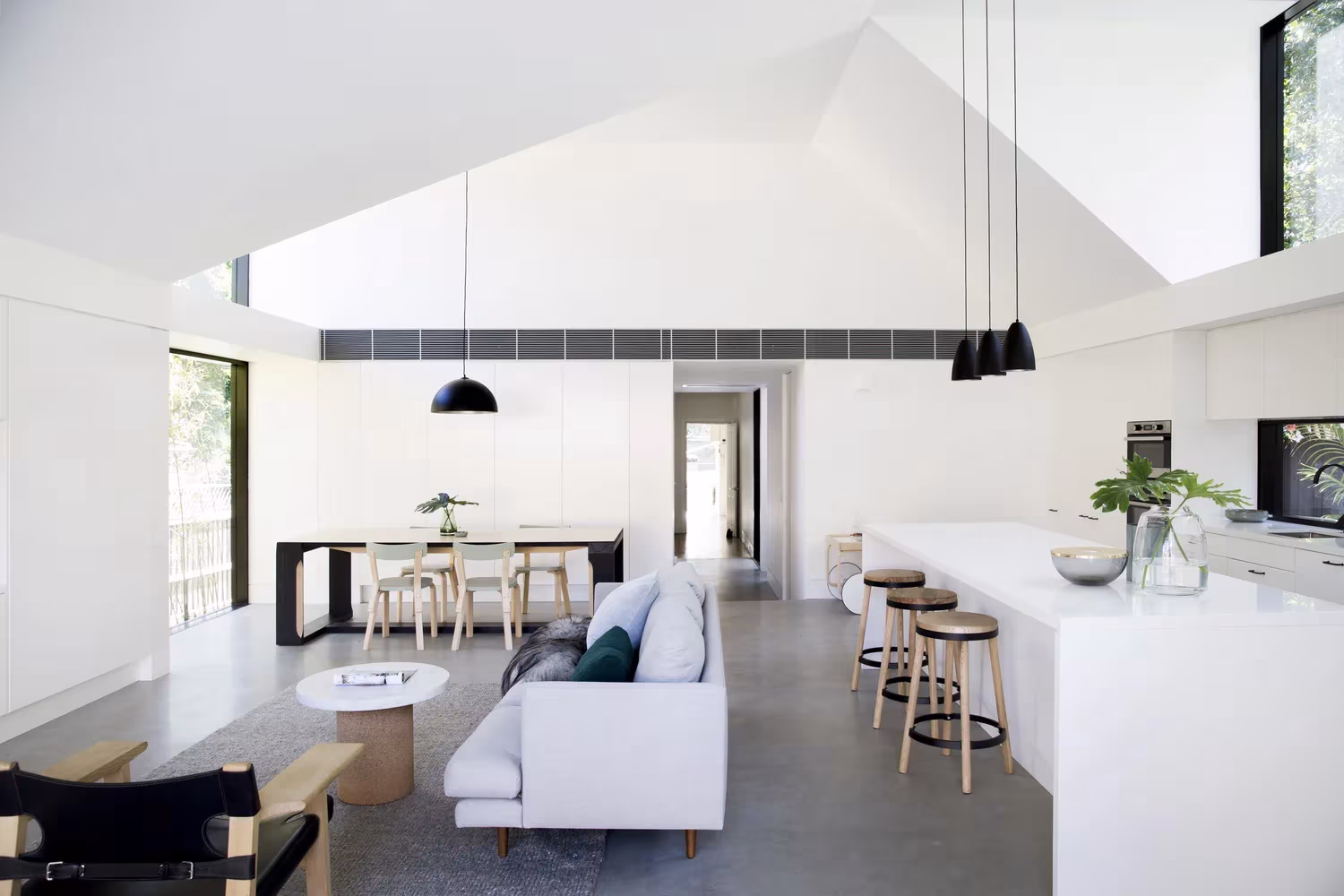 Salón, cocina y comedor bajo un techo de doble altura con lámparas negras en la Allen Key House de Sídney