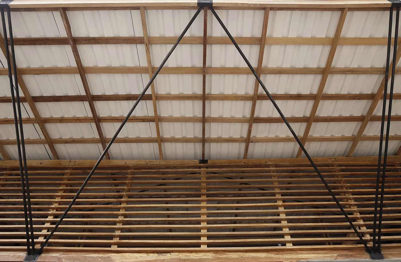 Cubierta de chapa con estructura de madera y tirantes de acero vista desde dentro en la Casa de Oración, Ecuador