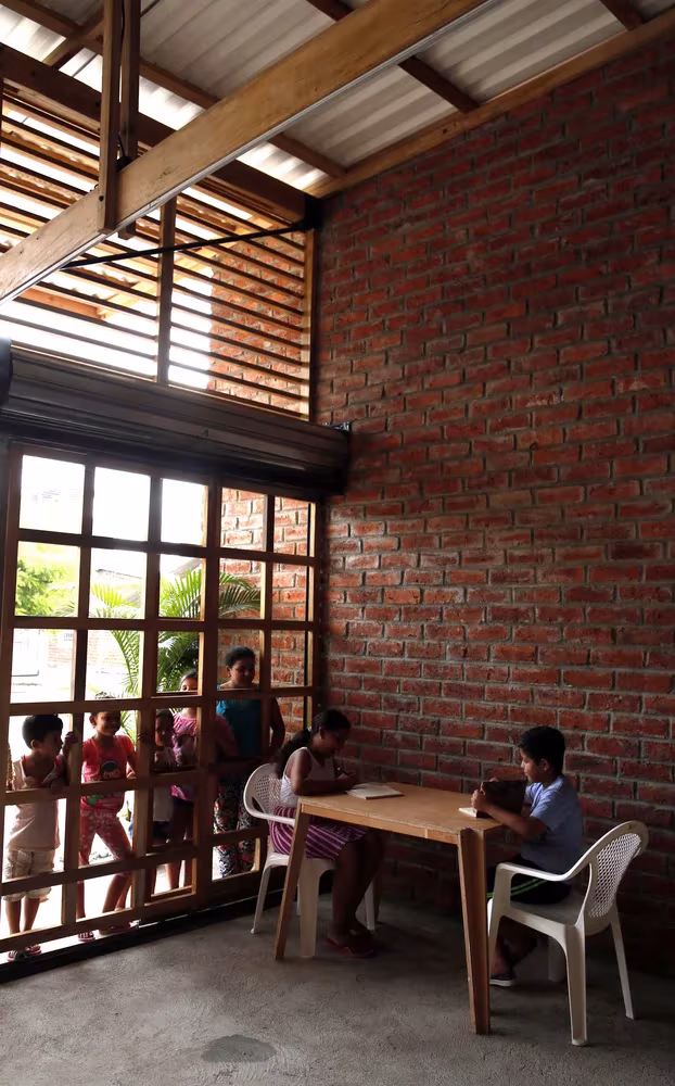 Niños en una mesa junto a la celosía de madera y el muro de ladrillo de la Casa de Oración, Babahoyo, Ecuador