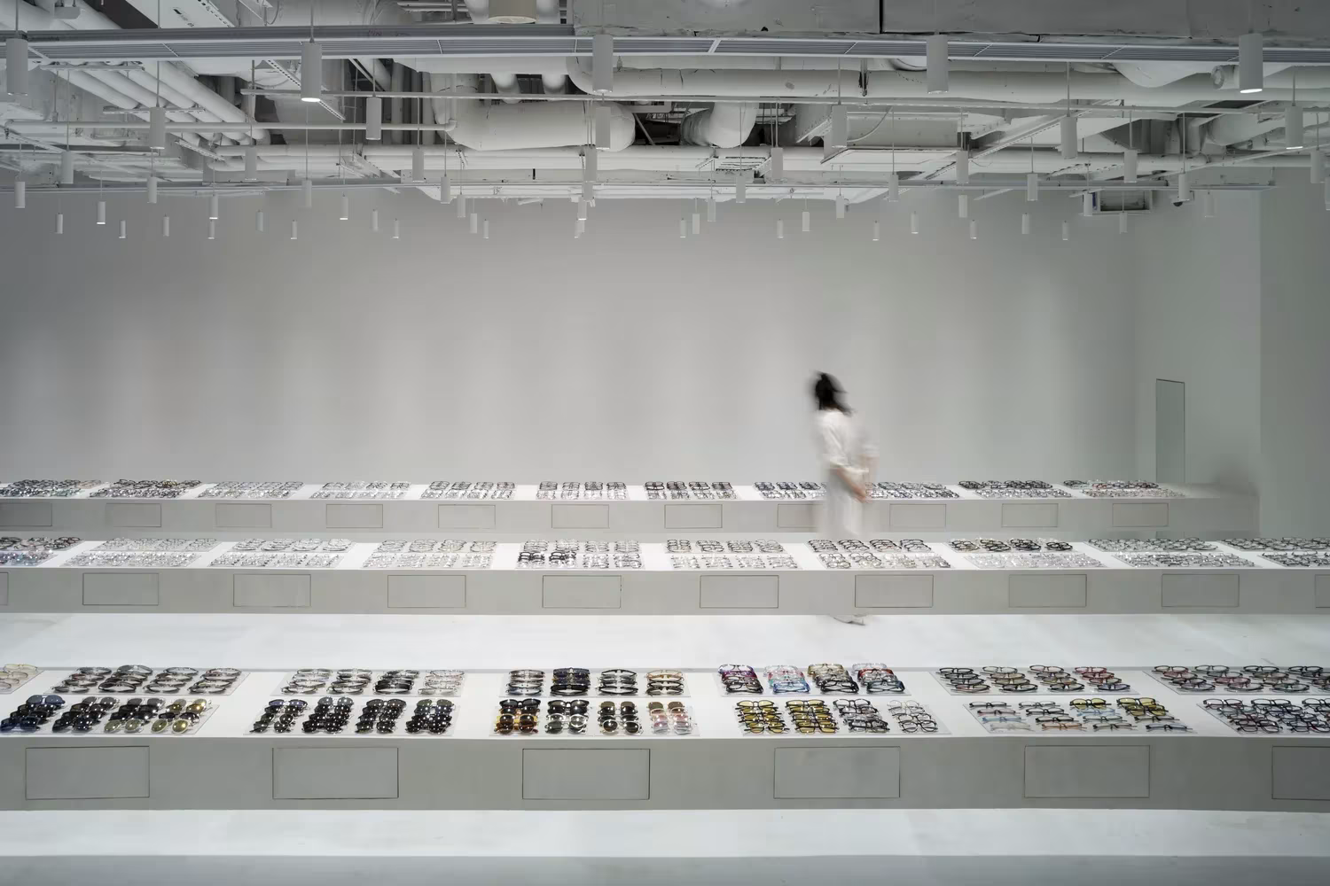 Tienda JINS de Junya Ishigami en Shanghái, con mesas blancas en voladizo cargadas de gafas en un espacio diáfano