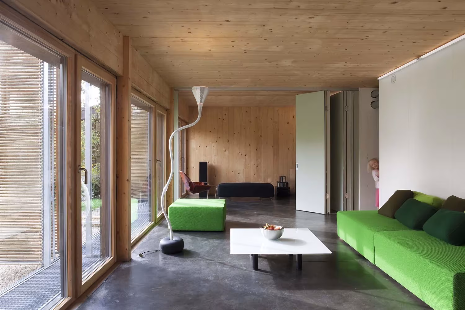 Sala de estar de techo de madera y grandes cristaleras con sofás verdes en la Maison Bambou de Karawitz Architecture
