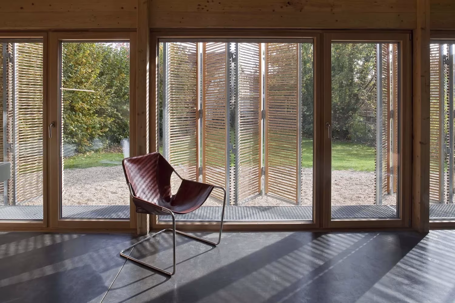 Sillón de cuero y cristaleras con contraventanas de bambú sobre suelo oscuro en la Maison Bambou, Bessancourt