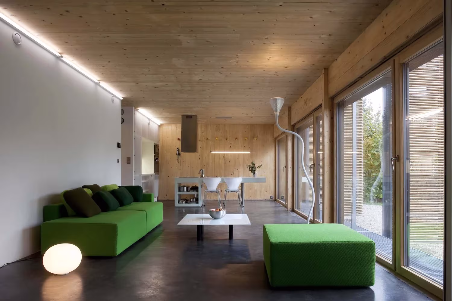 Salón de la Maison Bambou con sofás verdes, suelo de hormigón pulido y cristaleras con celosía de bambú, Bessancourt