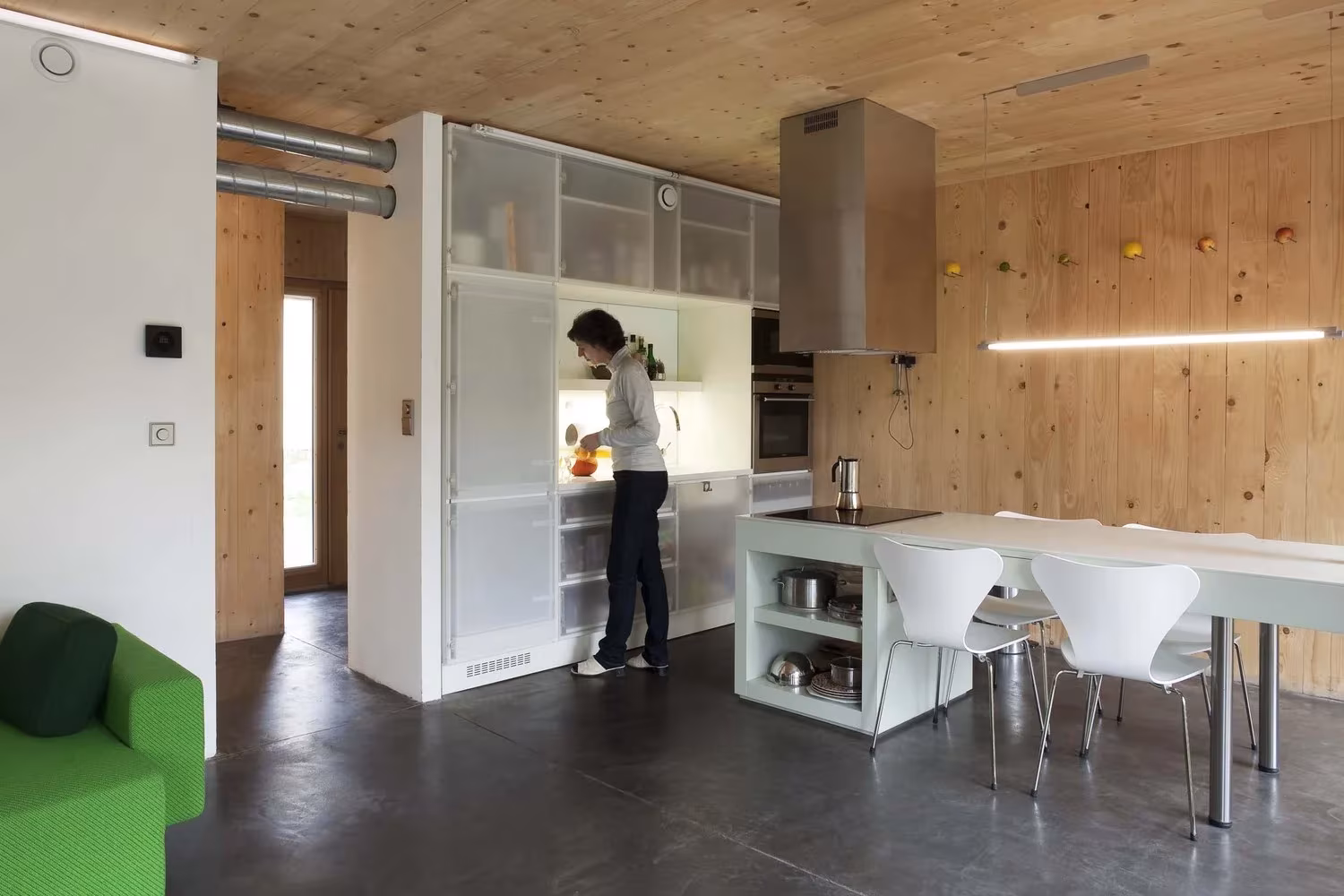Cocina con isla blanca, mesa larga y paredes de madera en la casa pasiva Maison Bambou de Karawitz, Bessancourt