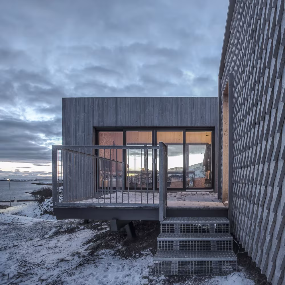 Cabaña de madera gris con terraza acristalada y escalera sobre la nieve en Fleinvær, de Tyin Tegnestue y Rintala Eggertsson