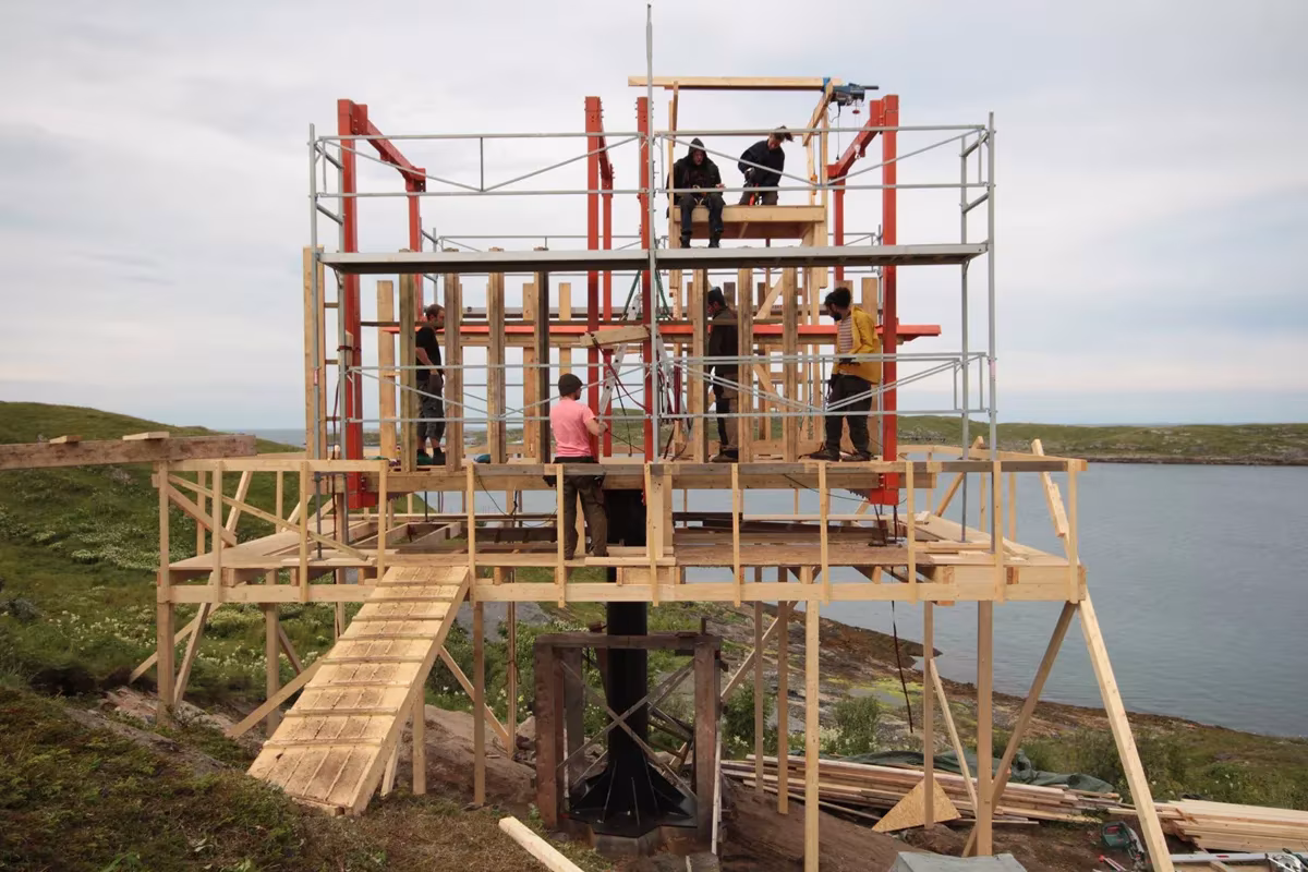 Andamios y estructura de madera de una cabaña de Fleinvær sobre pilotes en construcción, con obreros trabajando
