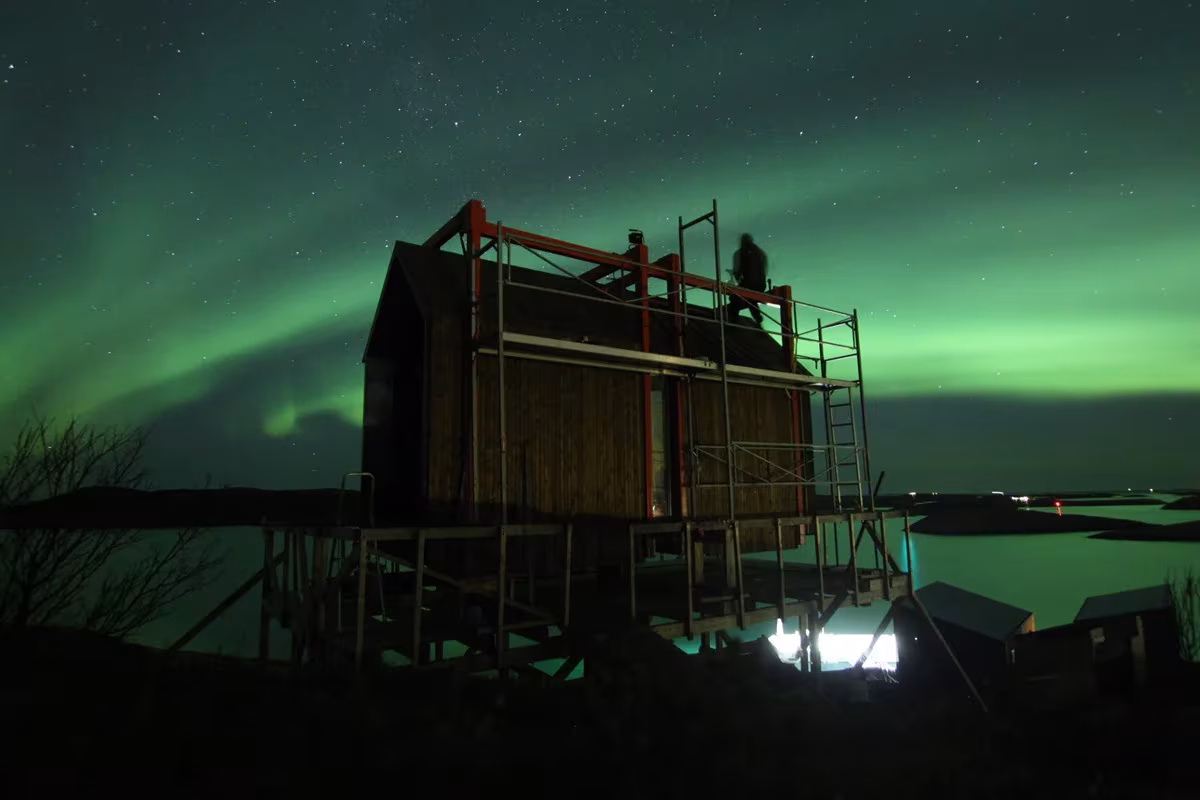 Cabaña de Fleinvær en obra bajo una aurora boreal verde sobre el mar de Noruega