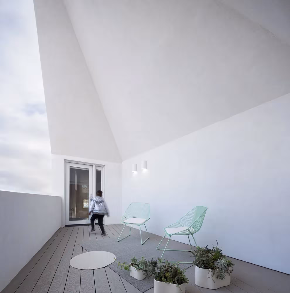 Terraza de la Haus Gables con suelo de madera, sillas verdes y un hastial blanco que enmarca el cielo, Atlanta