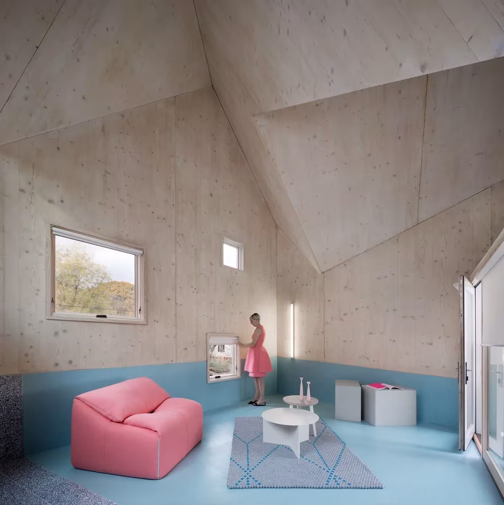 Sala de estar de madera con suelo azul, sillón rosa y cubierta de planos inclinados en la Haus Gables, Atlanta
