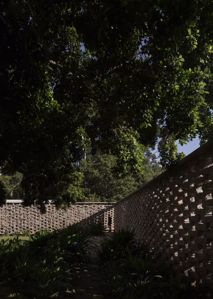 Muro de ladrillo calado de la Capilla Ingá-mirim entre la vegetación y las ramas de un gran árbol, São Paulo