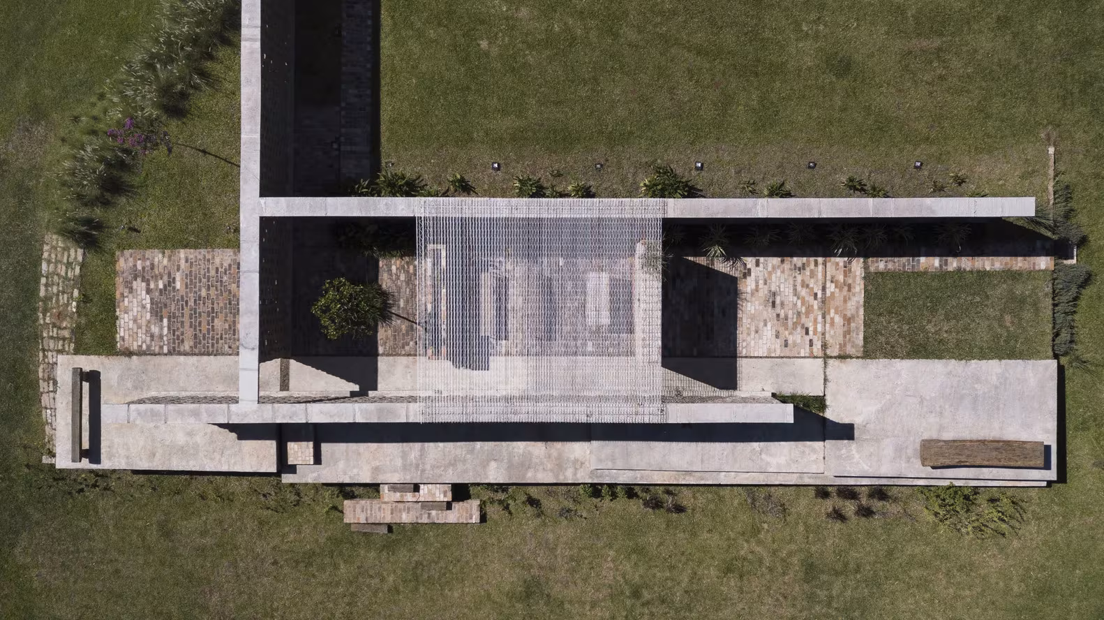 Vista cenital de la Capilla Ingá-mirim de messina | rivas, con sus muros en L de hormigón y ladrillo sobre el césped