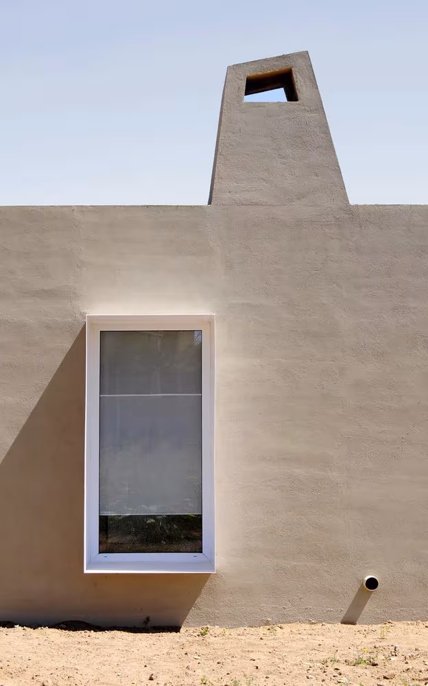 Ventana vertical de marco blanco y chimenea sobre el muro de revoco de la casa de NUA Arquitectures en Botarell