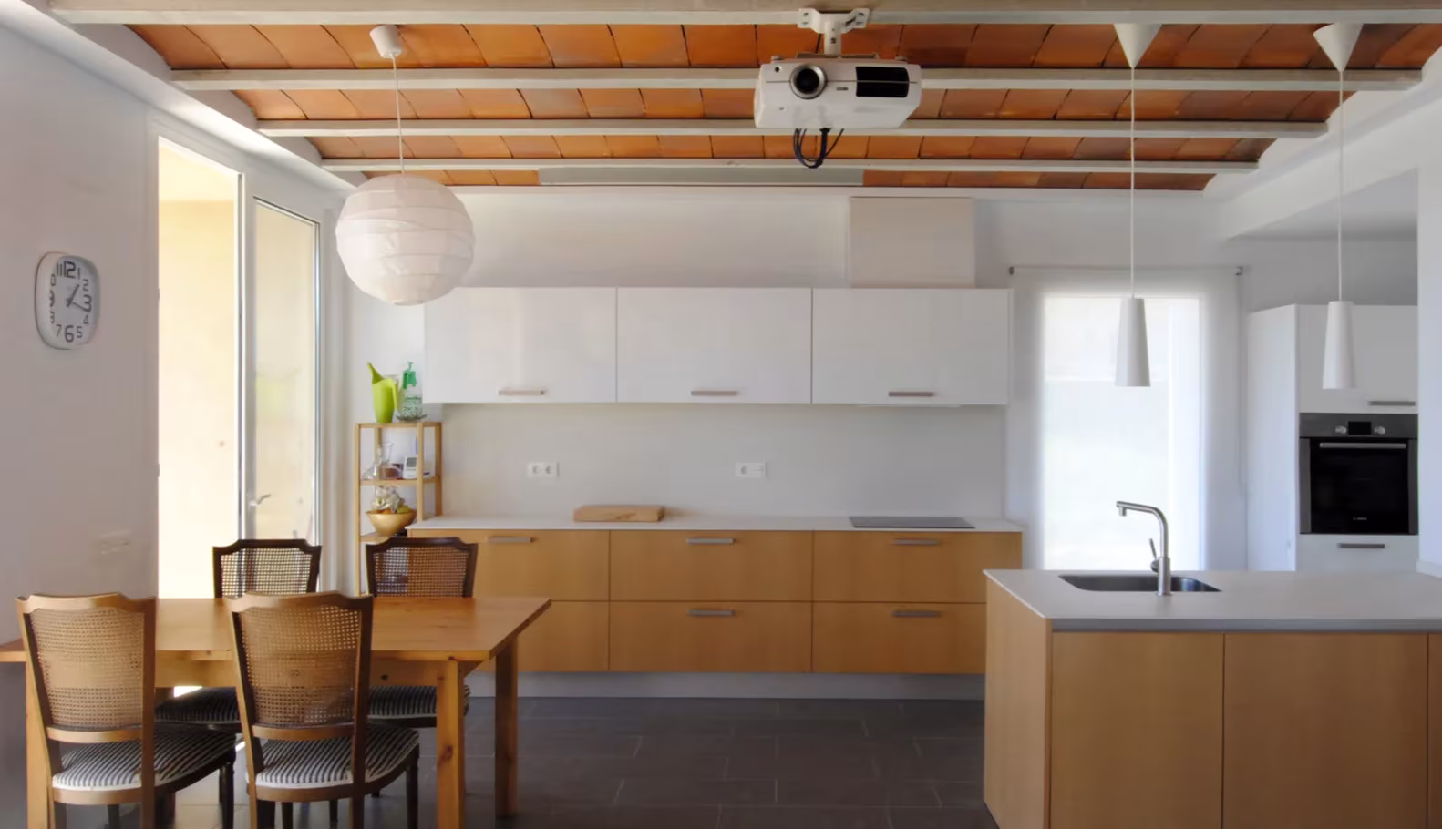 Cocina con isla y muebles de madera bajo un techo de vigas y bovedilla cerámica en la casa de Botarell, Tarragona