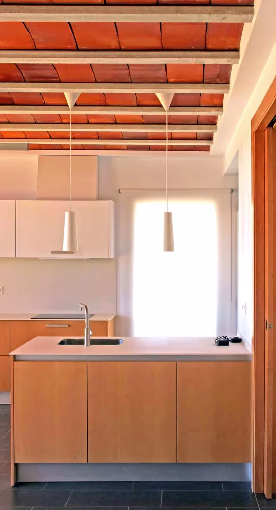 Isla de cocina de madera y encimera clara bajo el techo de vigas con bovedilla cerámica en la casa de Botarell
